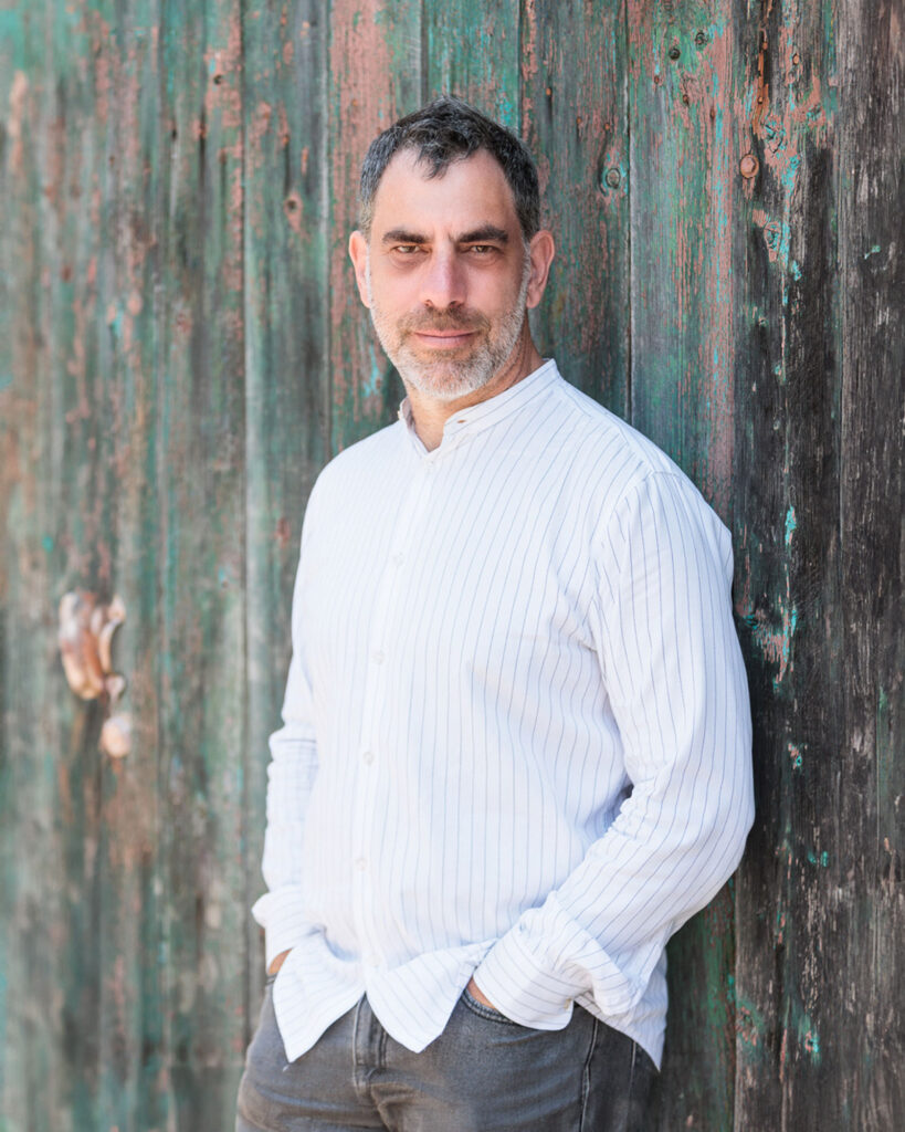 Jonni Super, Toronto Bar Mitzvah, wedding and portrait photographer, standing against a rustic wooden backdrop.